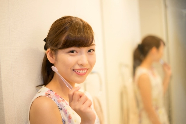 歯ブラシを頬にあてる笑顔の女性