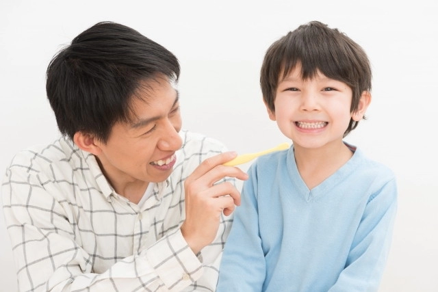 父親に歯磨きをしてもらう男の子