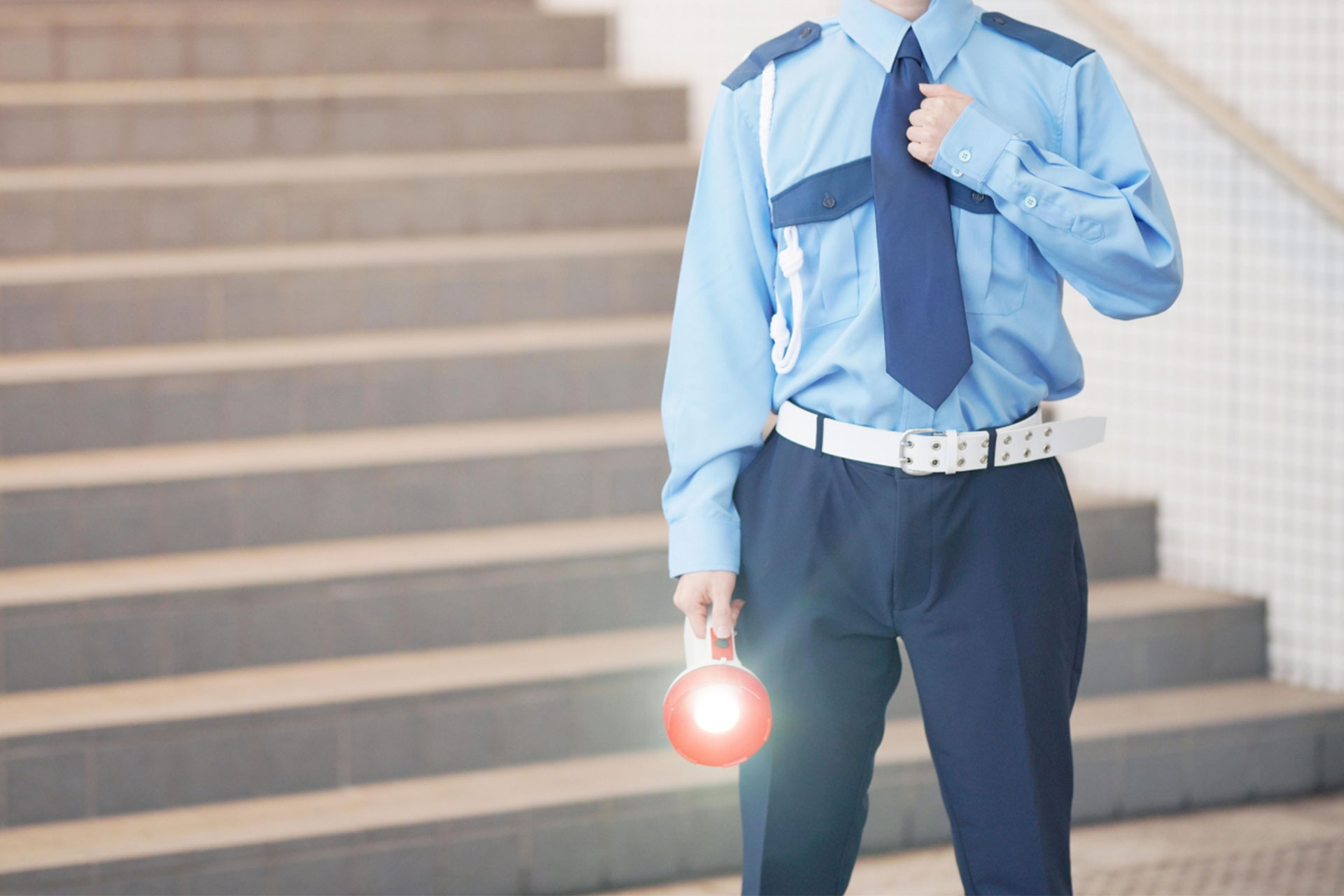 警備員が交通誘導のため赤い誘導灯を掲げる様子