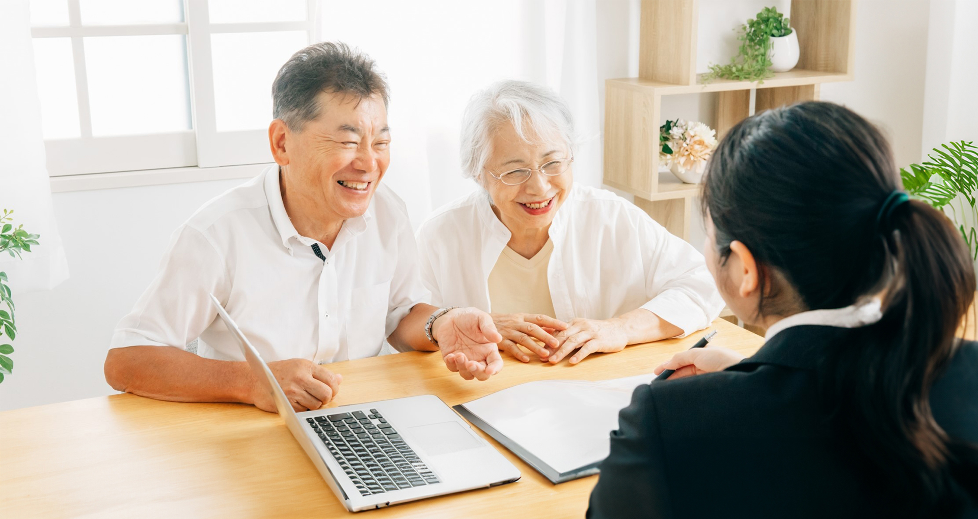高齢の夫婦が明るい部屋で女性のコンサルタントと楽しく相談している様子