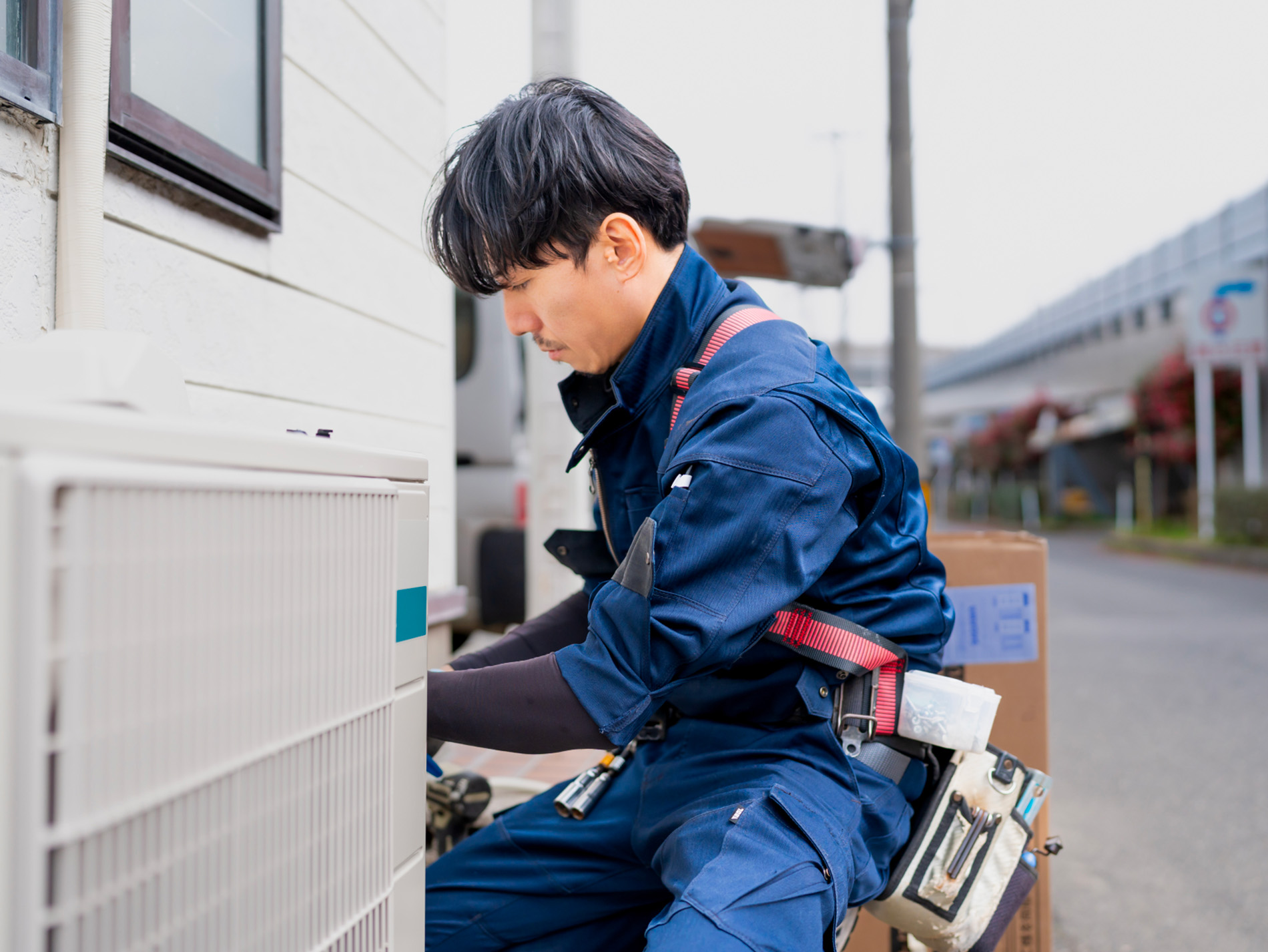 屋外でエアコンの室外機を点検する作業員