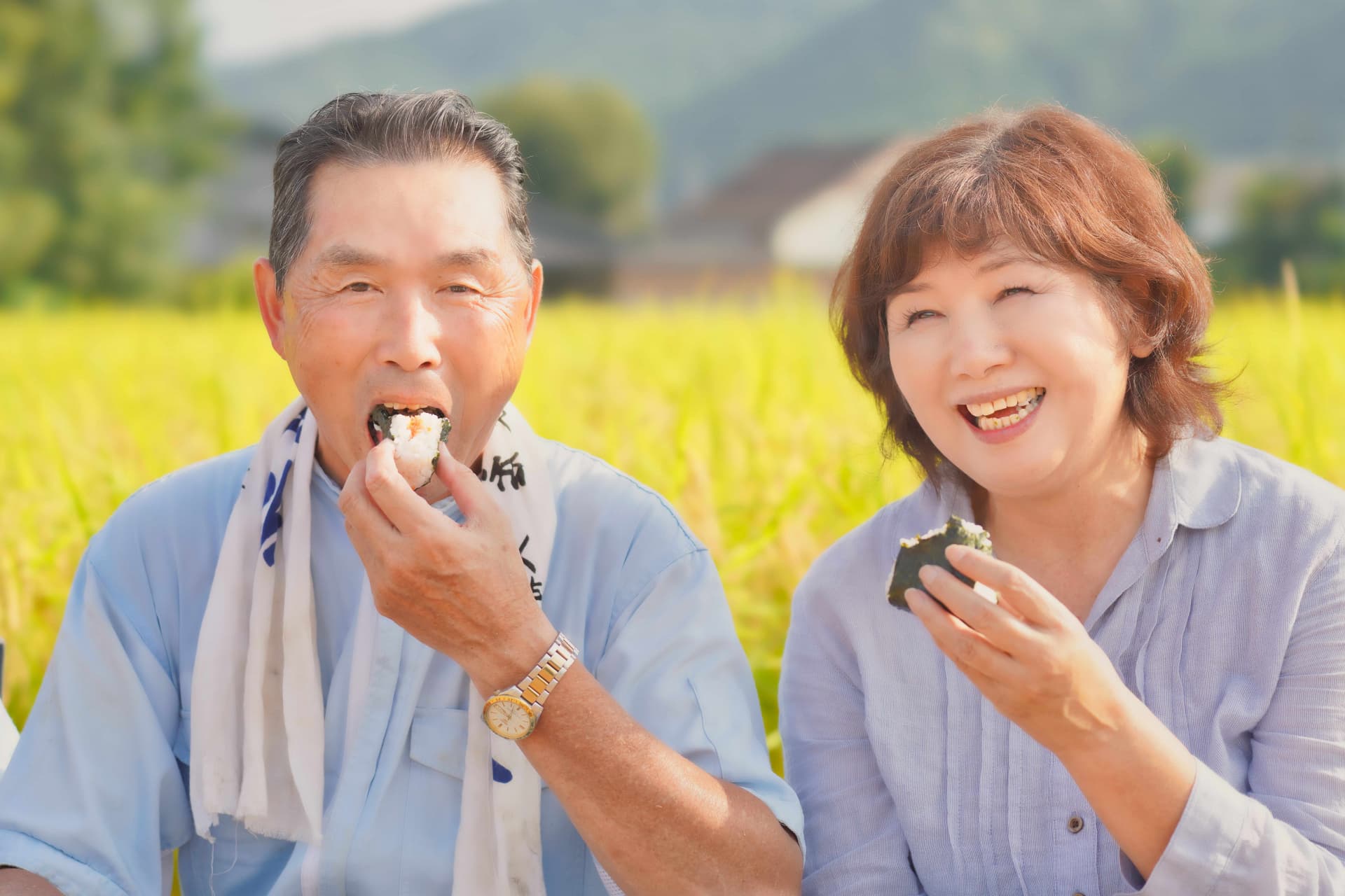 実りの田んぼでおにぎりを食べるご夫婦
