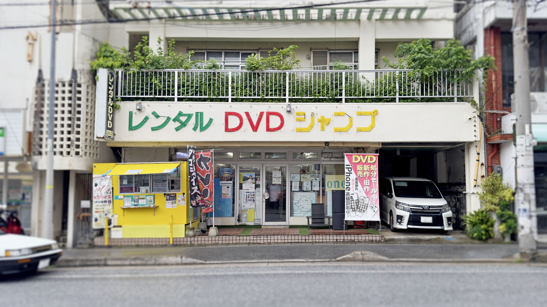 黄色・赤・緑の「レンタルDVDジャンプ」看板がある店舗外観